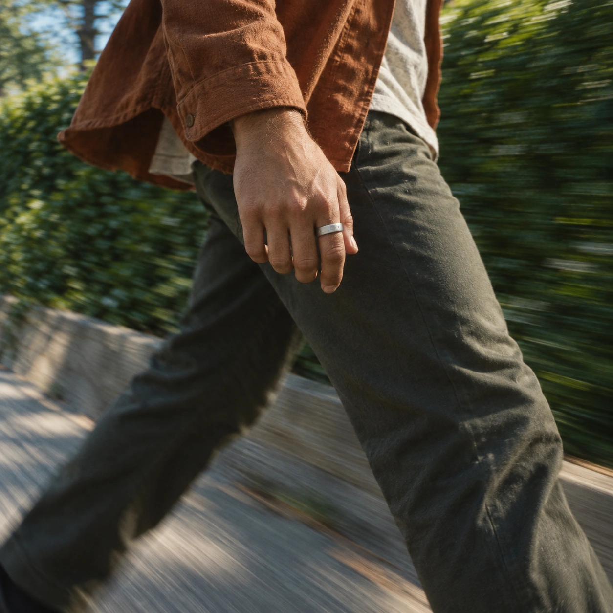 A close view of a walking stride and swinging hand wearing Interface, with green surroundings blurred by motion
