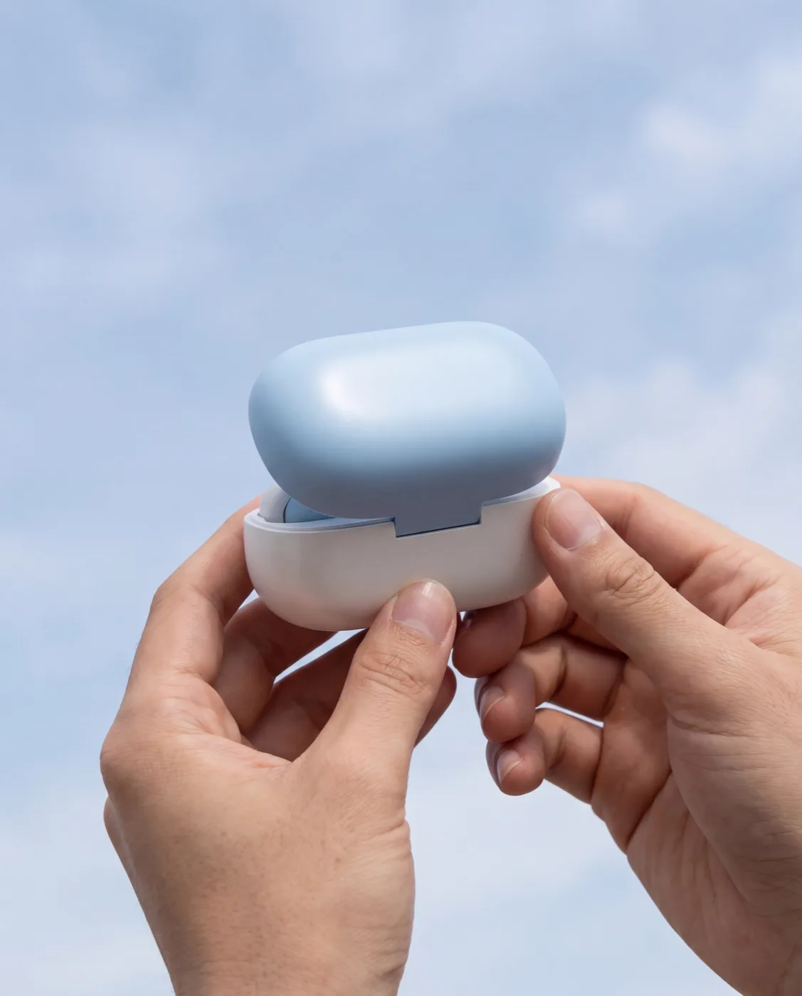 Two hands meeting against open sky, each holding a HumanPod